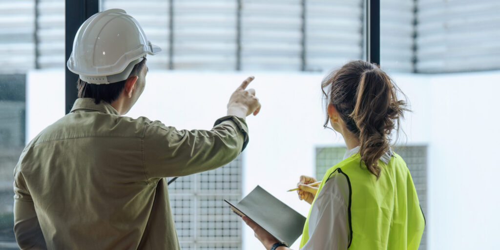 Two professional engineer and architect in safety helmet working together at construction site.