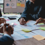 Groups of businesspeople working together as a team of analytics point to company graphs and charts to compare marketing strategies for new product offerings.