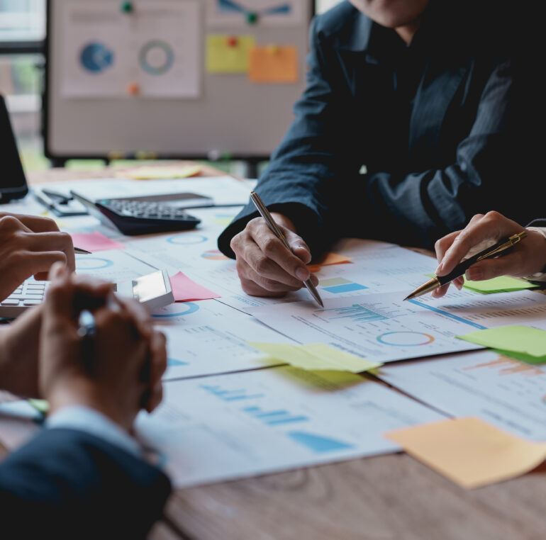 Groups of businesspeople working together as a team of analytics point to company graphs and charts to compare marketing strategies for new product offerings.