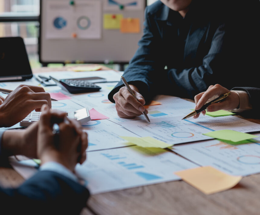 Groups of businesspeople working together as a team of analytics point to company graphs and charts to compare marketing strategies for new product offerings.