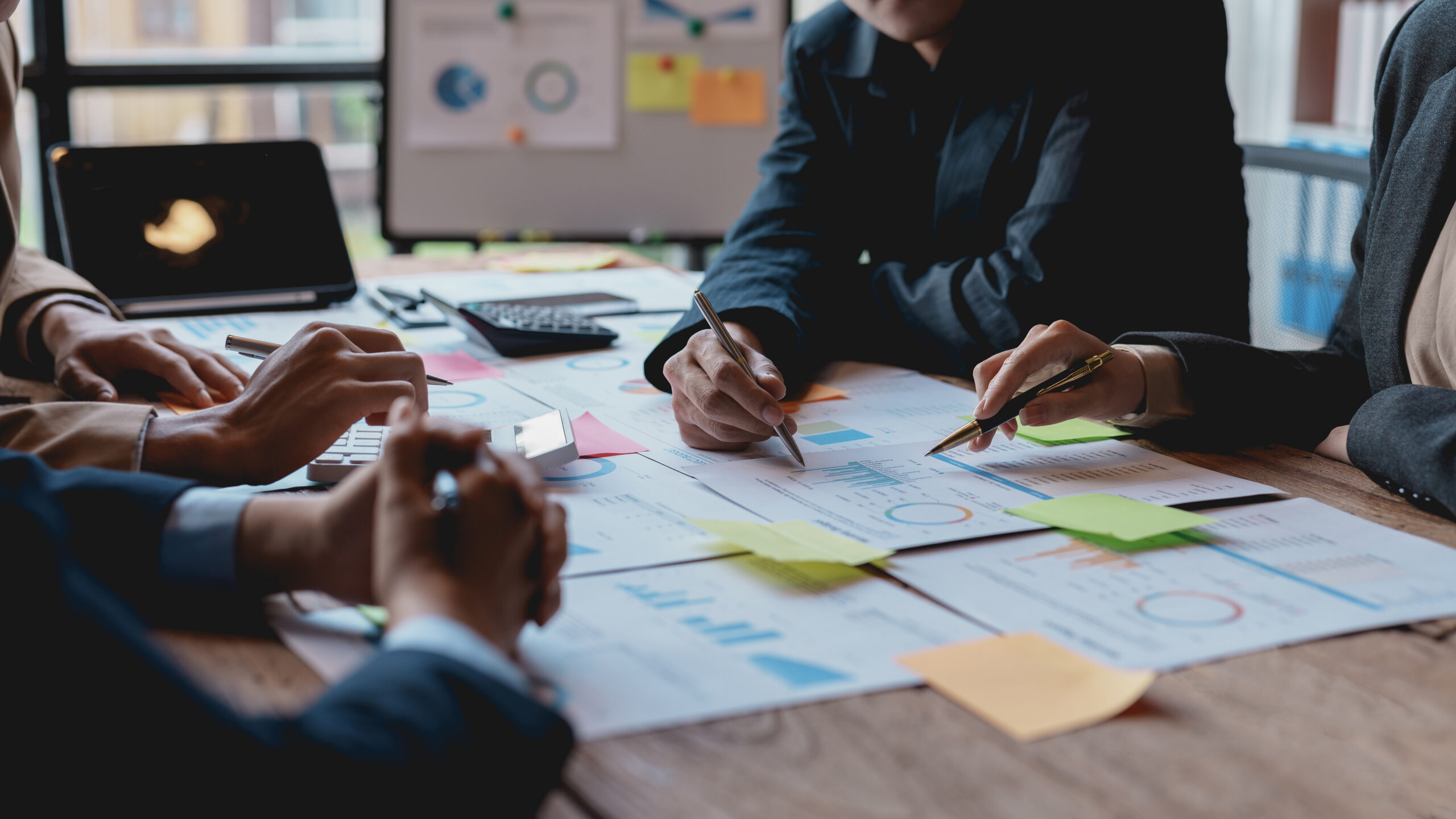 Groups of businesspeople working together as a team of analytics point to company graphs and charts to compare marketing strategies for new product offerings.