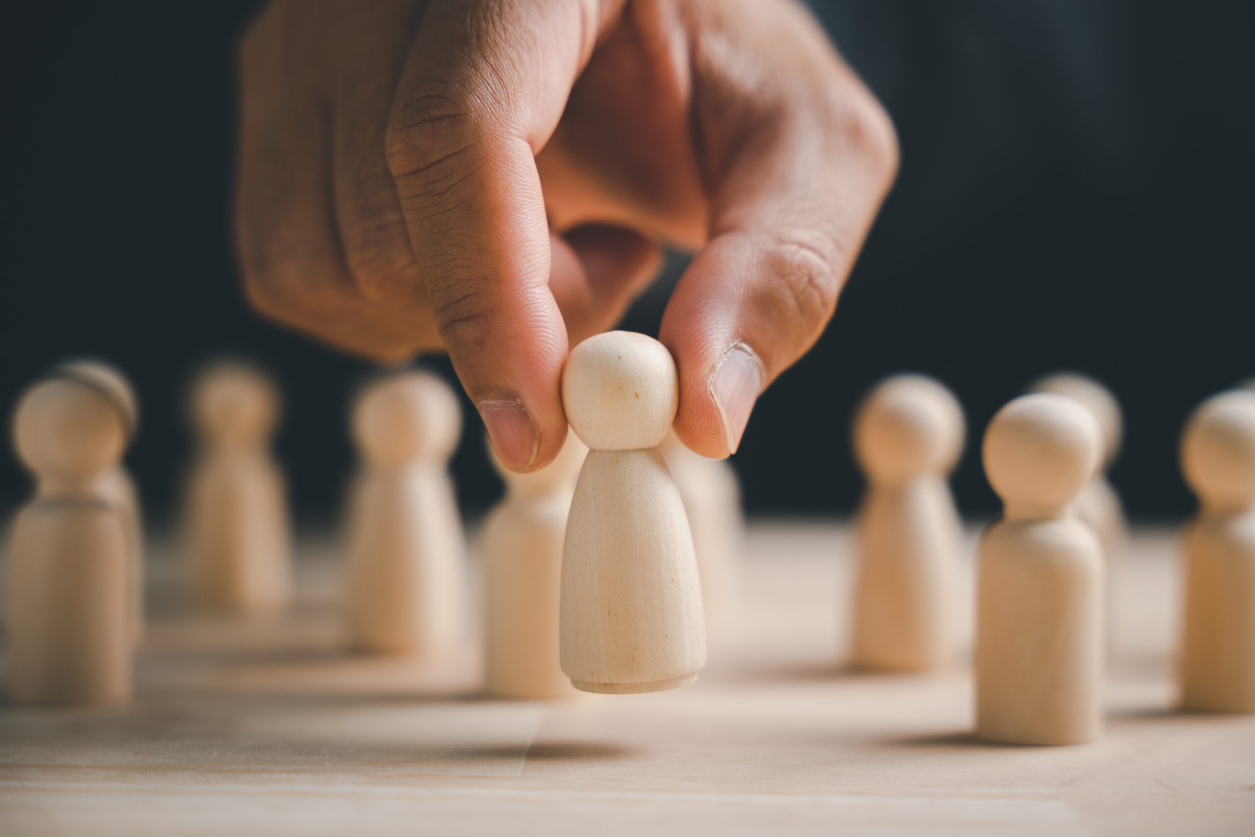 A hand carefully lifting a wooden figure from a group of figures.