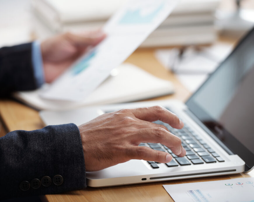 Close-up image of businessman checking documents and working on laptop, selective focus
