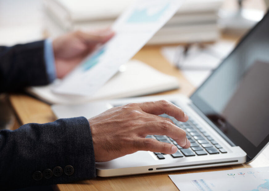 Close-up image of businessman checking documents and working on laptop, selective focus