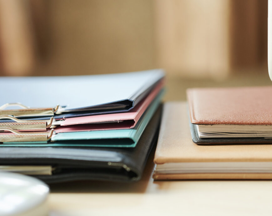 Stack of folders and planners on office desk, selective focus