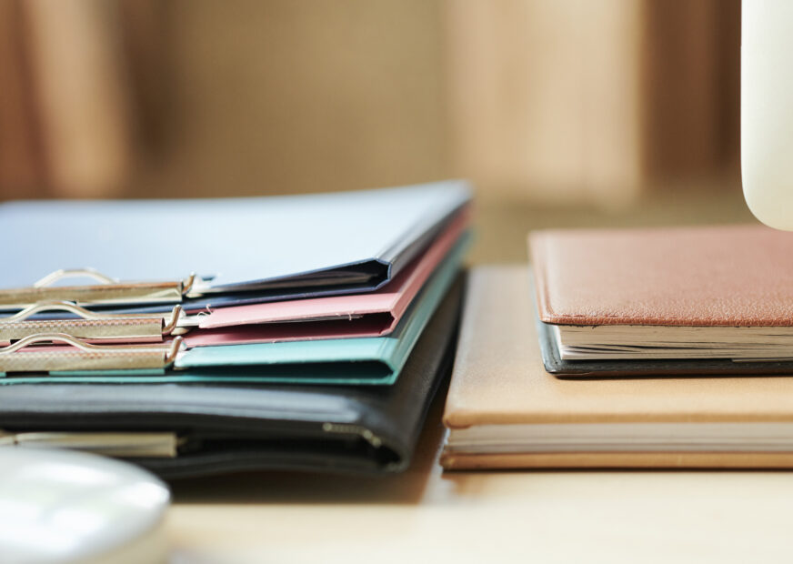 Stack of folders and planners on office desk, selective focus
