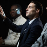 Caucasian businessman gesturing while speaking during panel discussion with diverse colleagues, presenting leadership and teamwork concepts. Useful for corporate communication or business event marketing