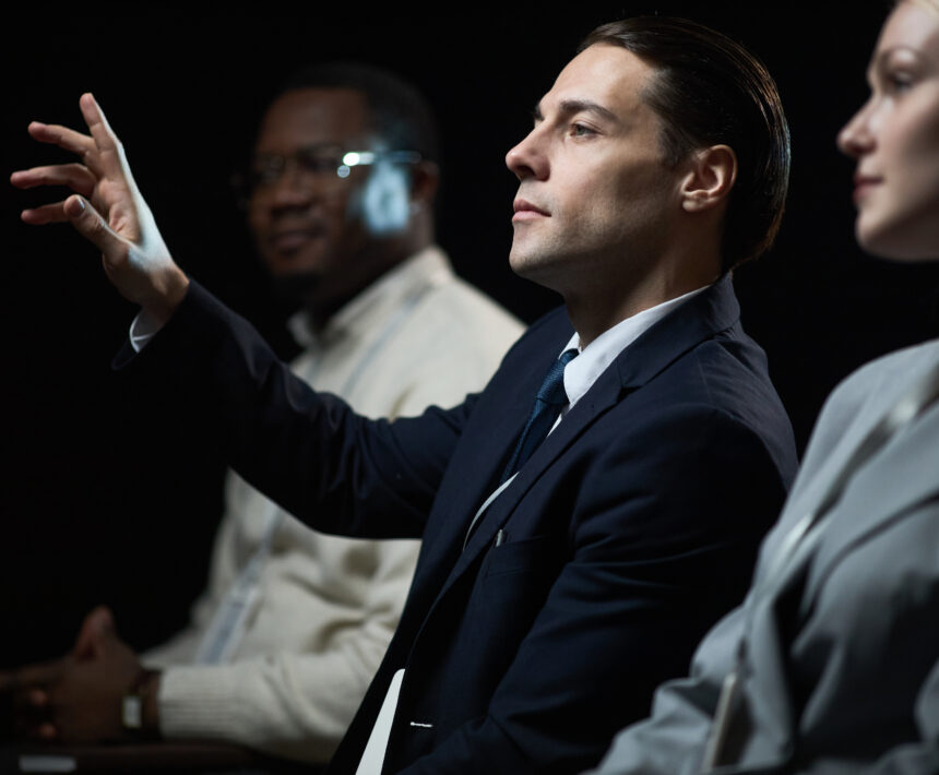Caucasian businessman gesturing while speaking during panel discussion with diverse colleagues, presenting leadership and teamwork concepts. Useful for corporate communication or business event marketing