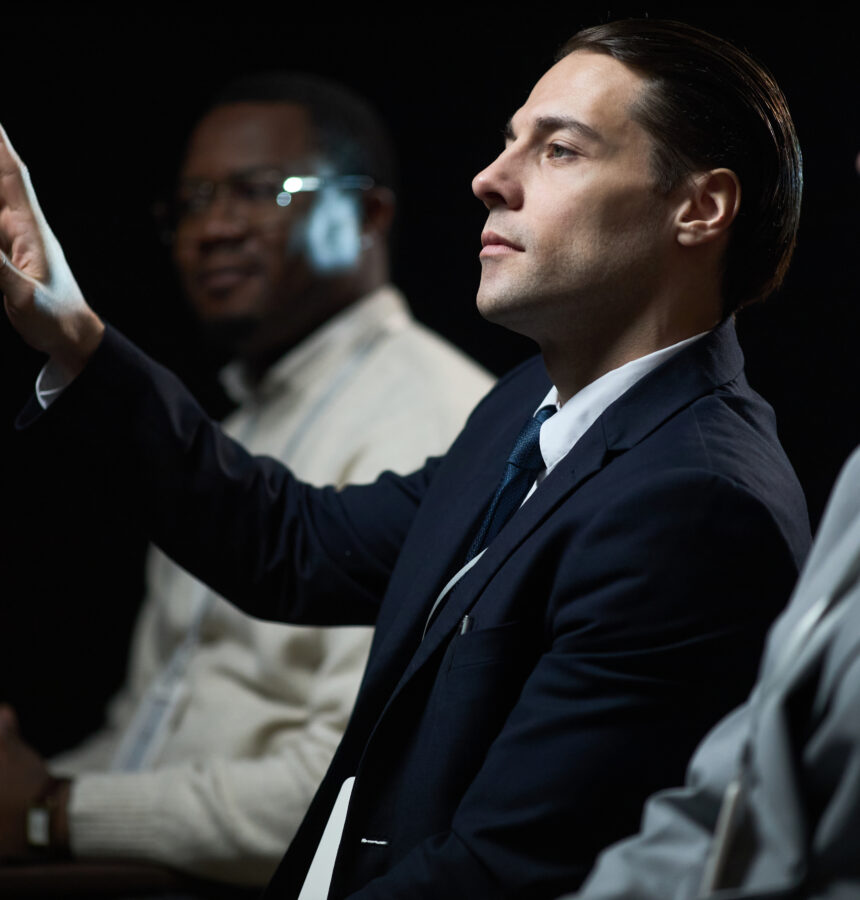 Caucasian businessman gesturing while speaking during panel discussion with diverse colleagues, presenting leadership and teamwork concepts. Useful for corporate communication or business event marketing