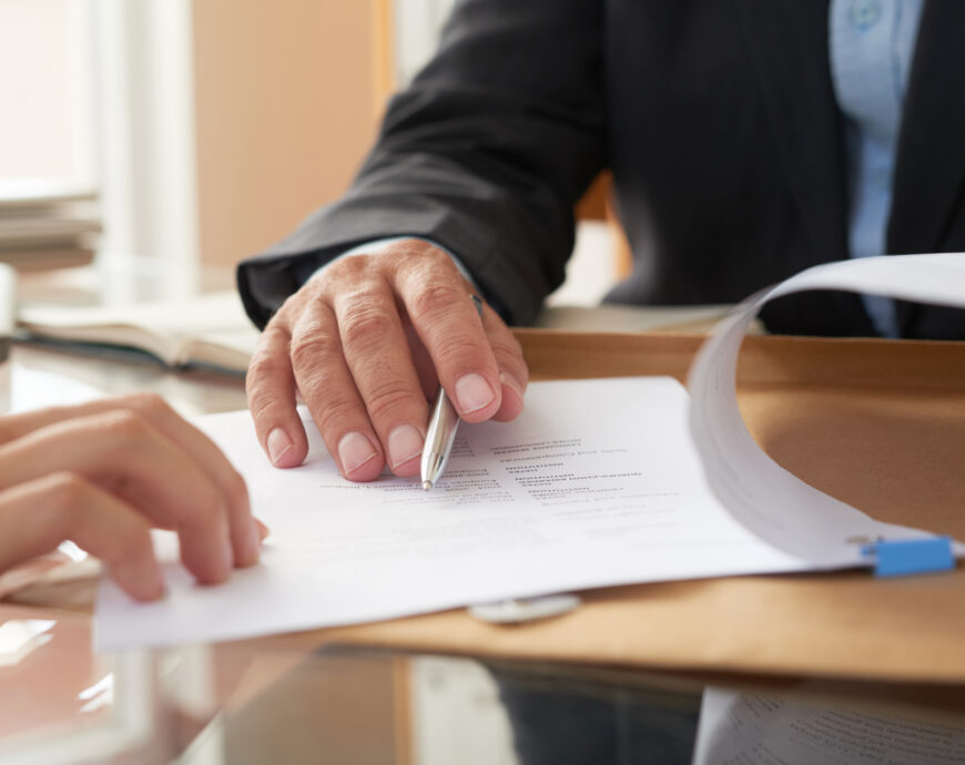 Close-up of businessman examining business contract and signing it at the office desk