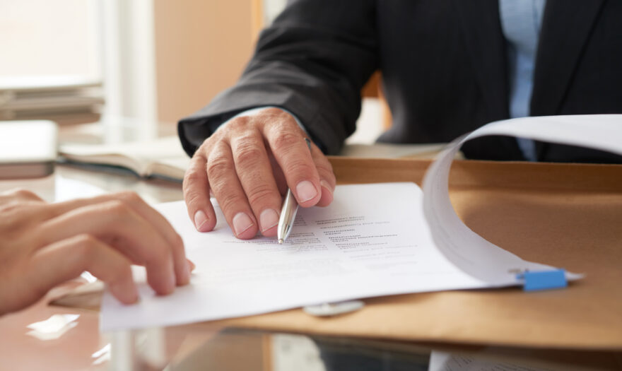 Close-up of businessman examining business contract and signing it at the office desk